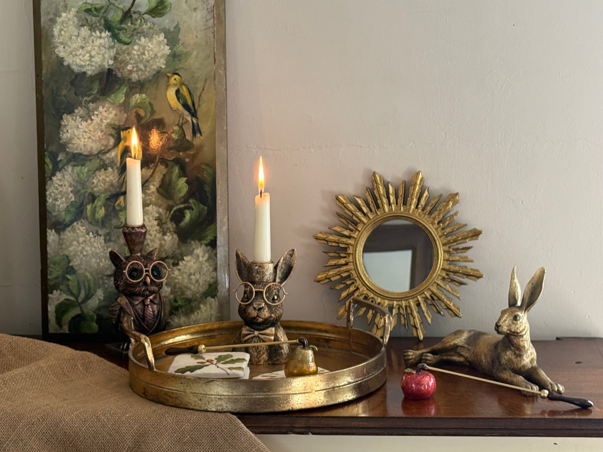 Autumn home décor display with gold woodland animal candle holders, a rabbit ornament, sunburst mirror, and tray styled on a wooden surface against a warm cosy background.