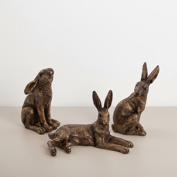 Three bronze rabbit sculptures on a light surface with a white background