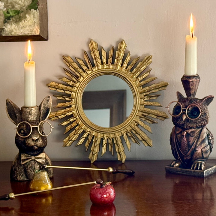 Decorative items including a rabbit-shaped candle holder, owl-shaped candle holder, and a sunburst mirror on a wooden surface.