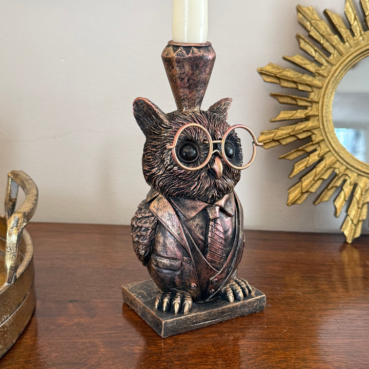 Bronze owl candle holder with glasses on a wooden surface, with a gold mirror in the background.