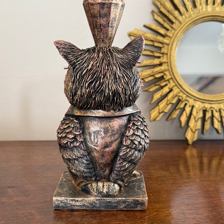 Bronze owl statue on a wooden surface with a decorative mirror in the background
