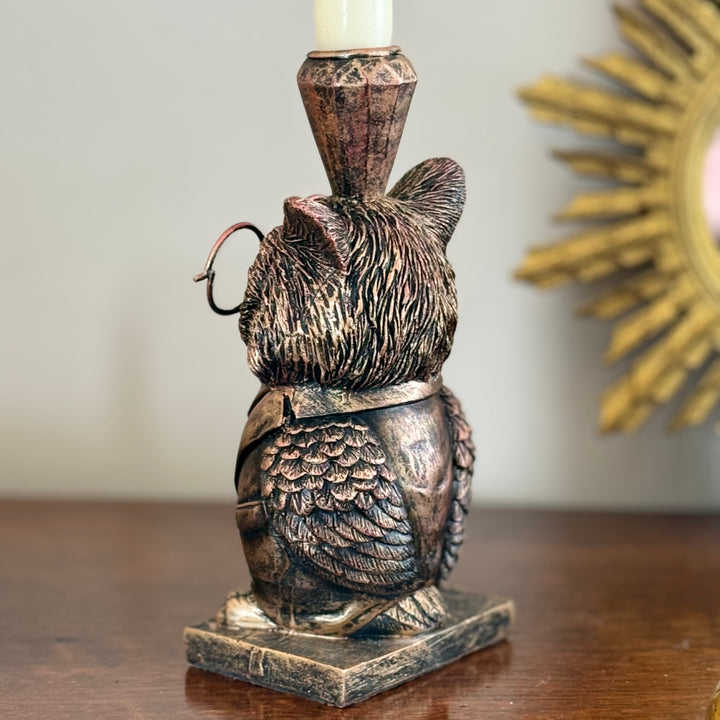 Bronze owl candle holder on a wooden surface with a blurred decorative mirror in the background.