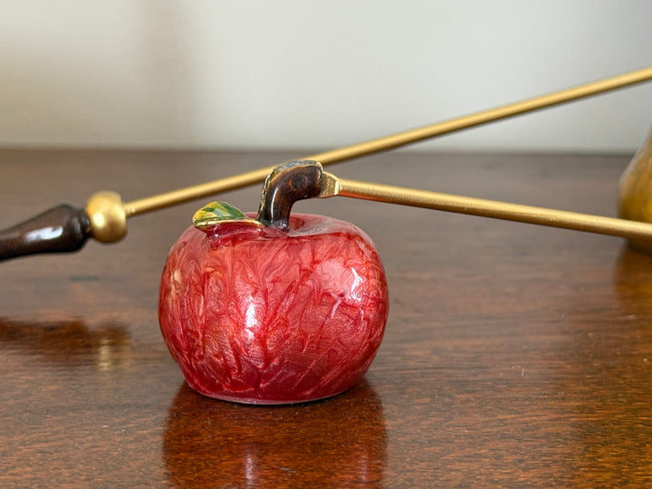 Red apple-shaped object with gold stem on a wooden surface