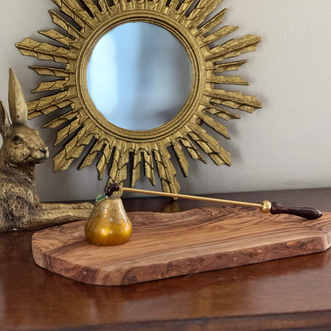 Decorative setup with a sun-shaped mirror, gold pear shaped candle snuffer on a wooden board, and rabbit sculpture on a table.