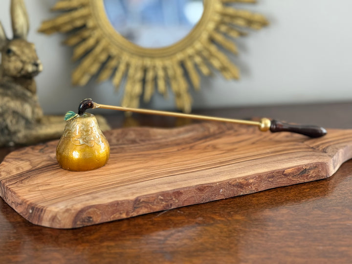 Wooden cutting board with a gold candle snuffer and decorative mirror in the background