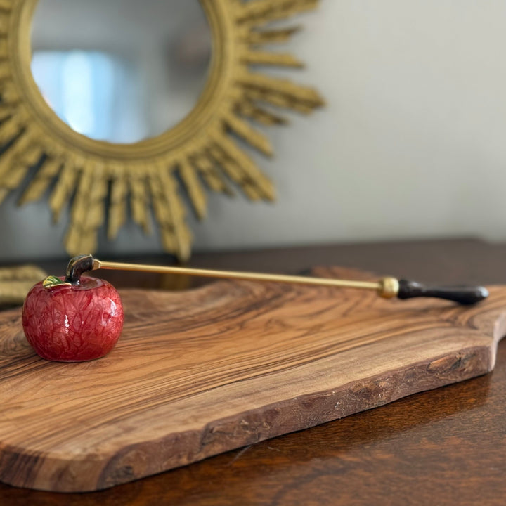 Small red apple candle snuffer  on a wooden surface with a decorative mirror in the background.