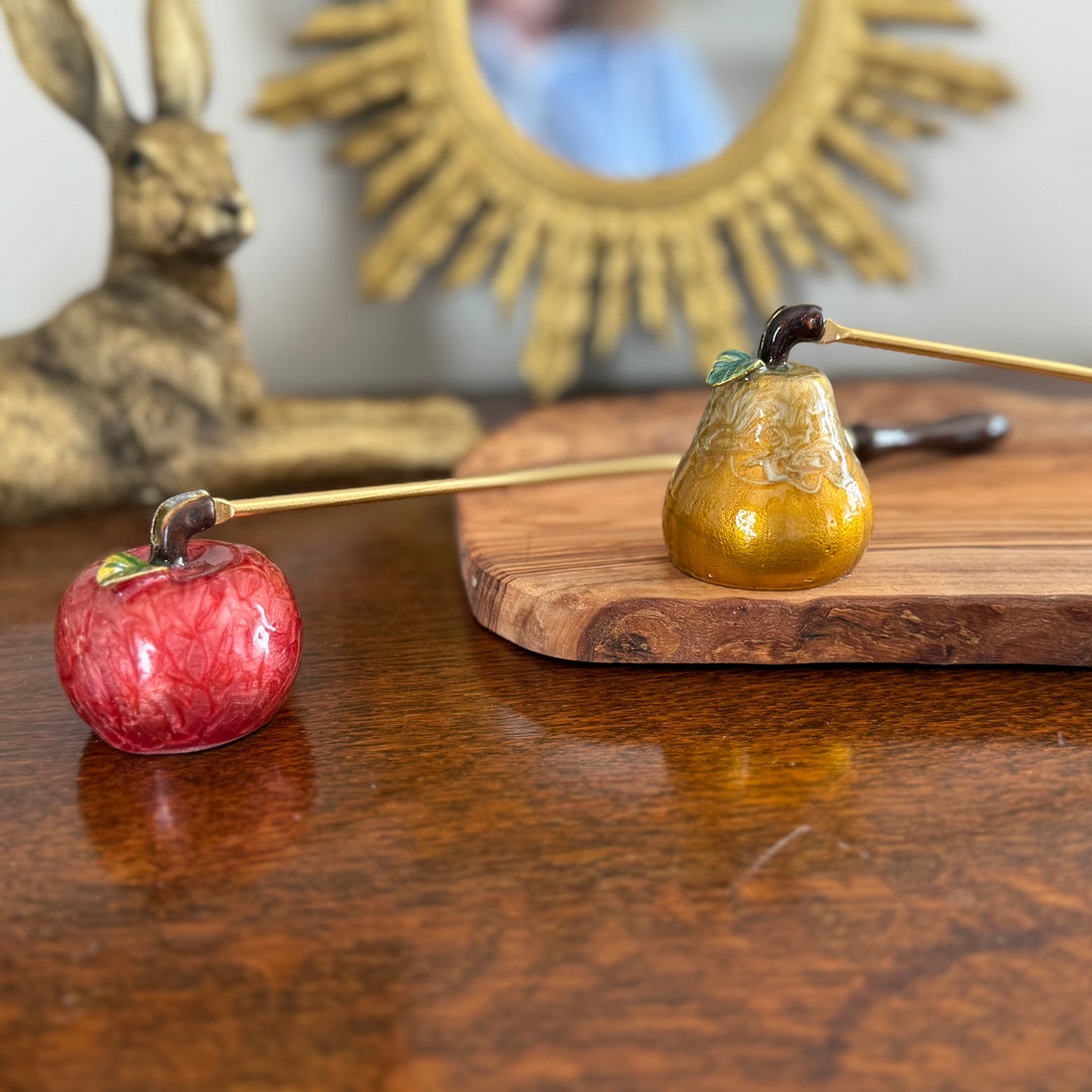 Decorative apple and pear-shaped candle snuffers  on a wooden surface with a rabbit figurine and mirror in the background.