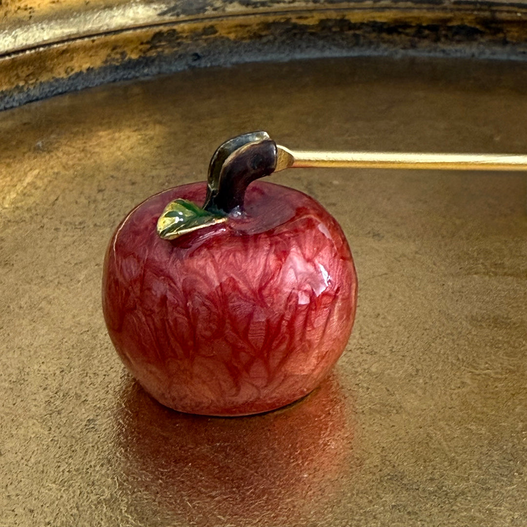 Red apple-shaped object with a gold stem on a reflective surface