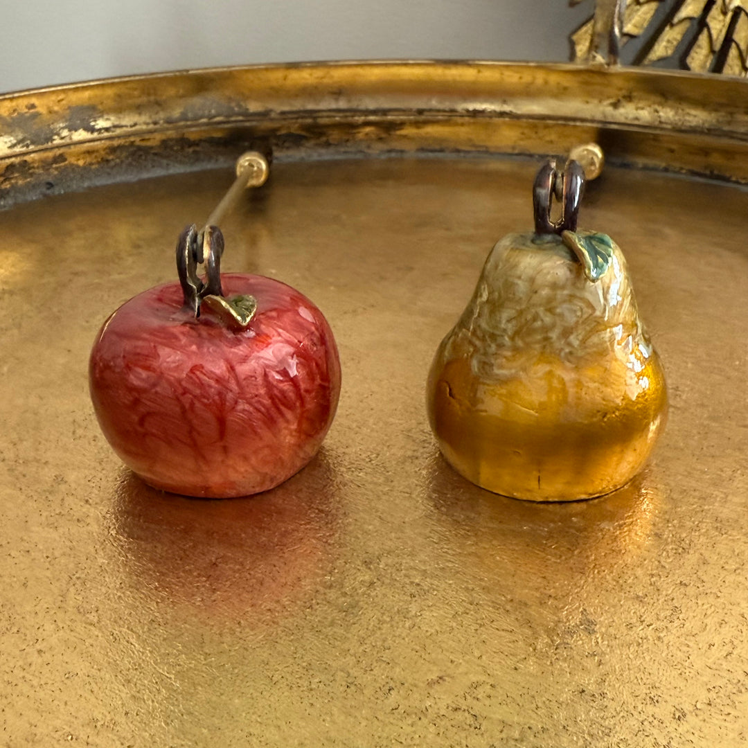Decorative apple and pear-shaped objects on a reflective gold surface