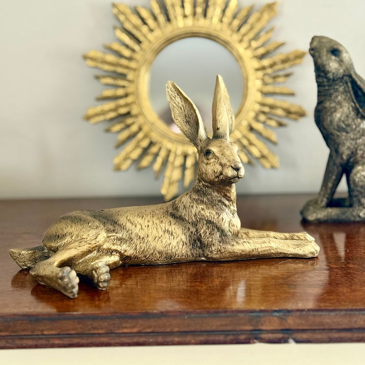 Gold rabbit statue on a wooden surface with a decorative sunburst mirror in the background.