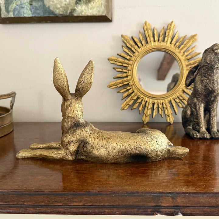 Gold rabbit sculpture on a wooden surface with a sunburst mirror in the background.