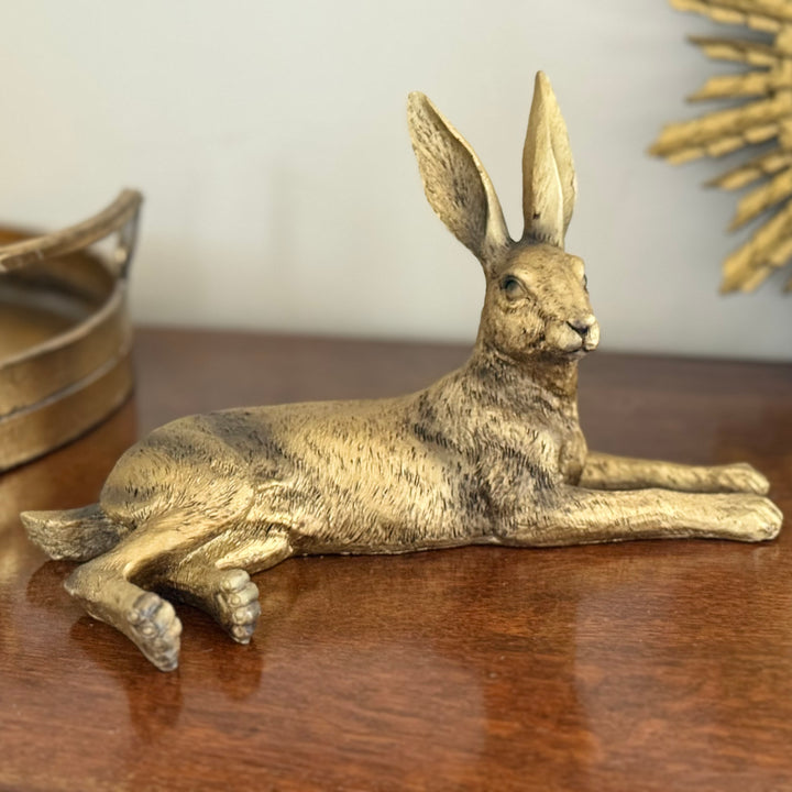 Bronze hare figurine on a wooden surface with a neutral background