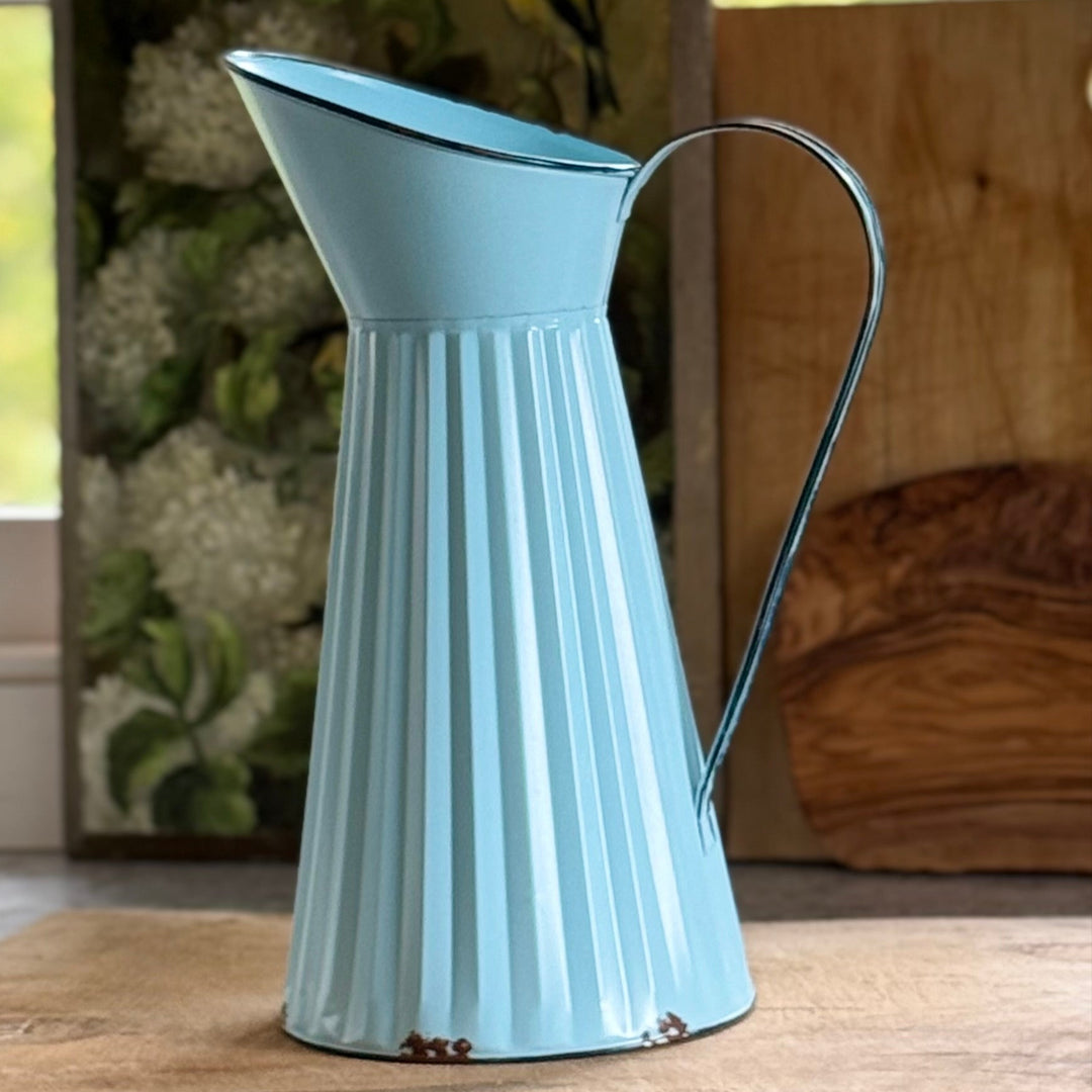 Light blue metal pitcher on a wooden surface with a blurred natural background