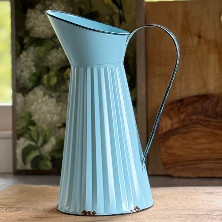 Light blue metal pitcher on a wooden surface with a blurred natural background