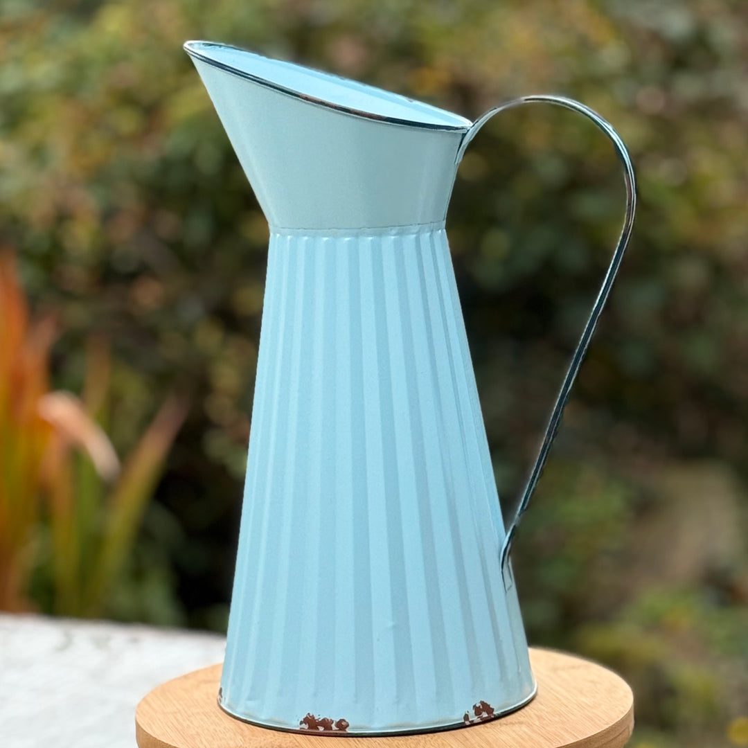Light blue metal  jug on a wooden stand with a blurred green background