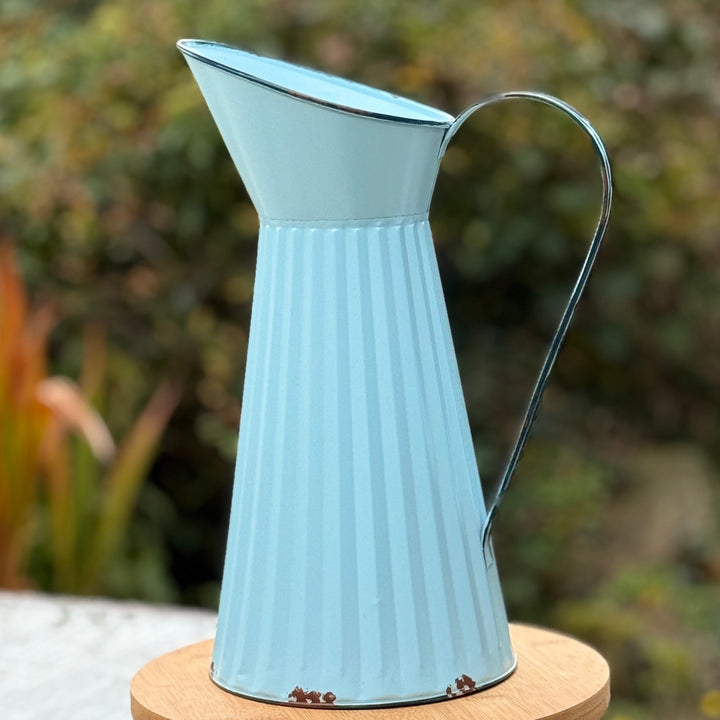 Light blue metal  jug on a wooden stand with a blurred green background