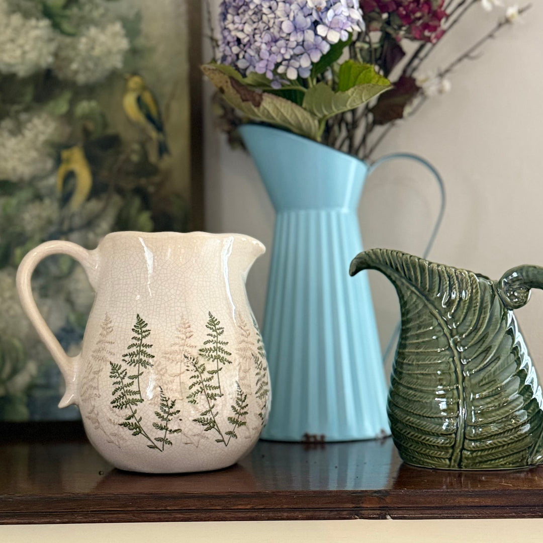 Three ceramic pitchers on a surface with a blurred floral arrangement in the background