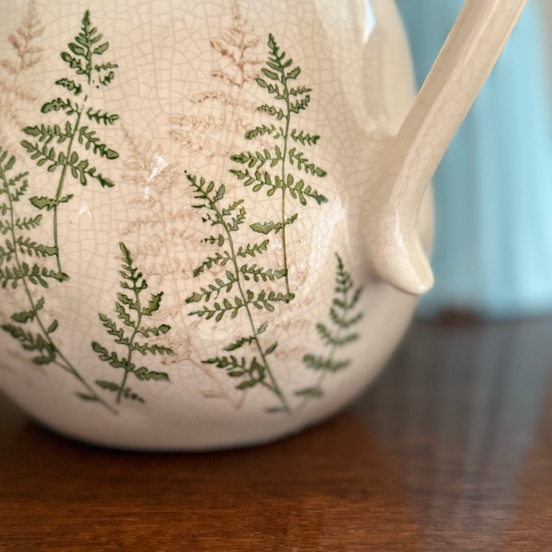 Close up of White ceramic jug with green leaf patterns on a wooden surface