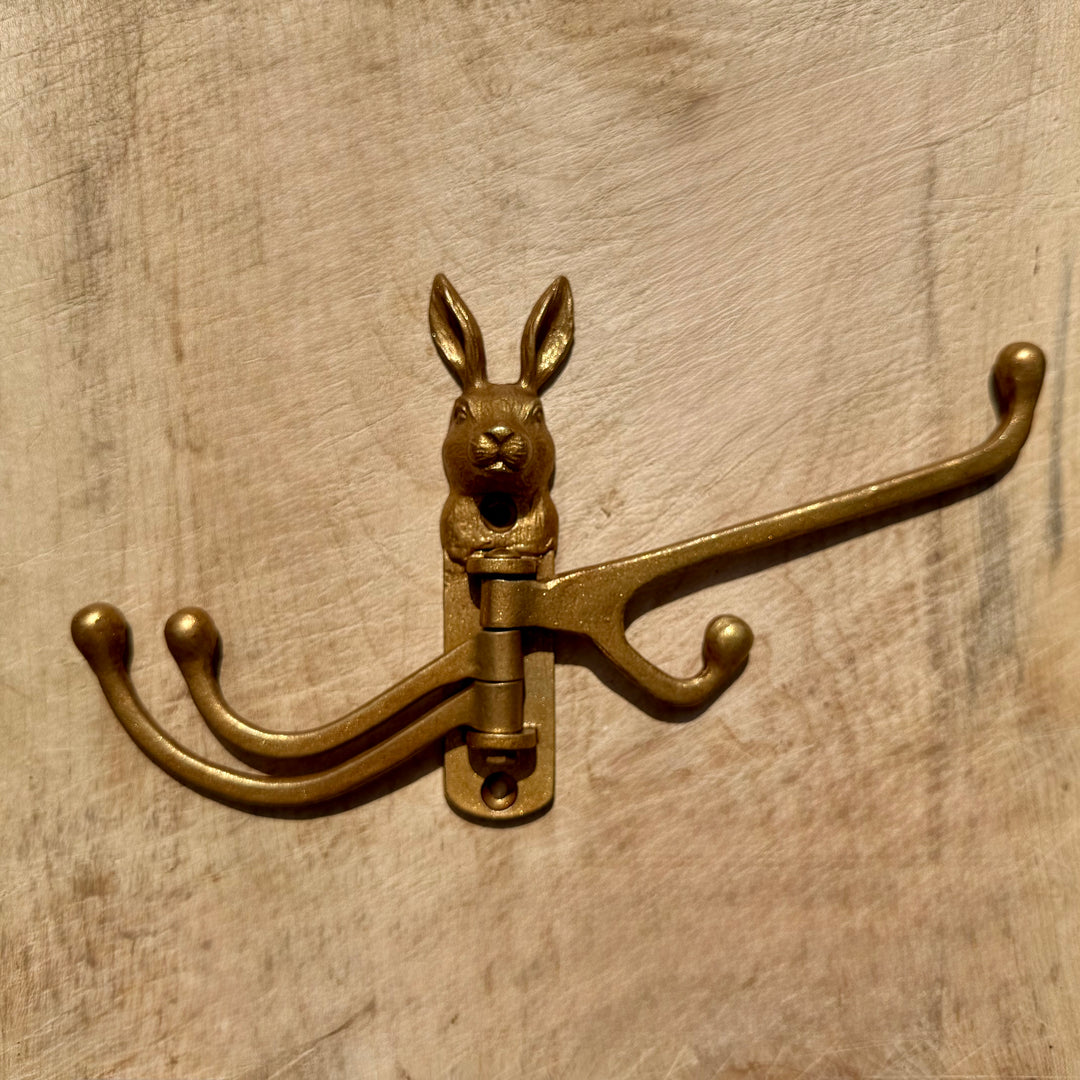A gold rabbit-shaped wall hook with three curved hanging arms, shown mounted on a light wood surface.