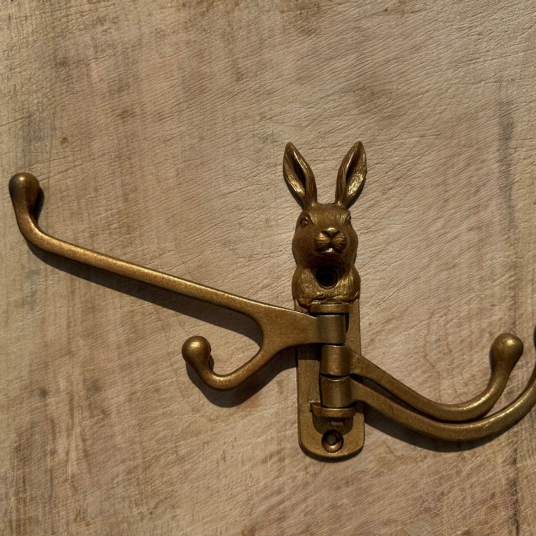 A vintage-style gold coat rack hook shaped like a rabbit head, mounted on a rustic wooden surface.