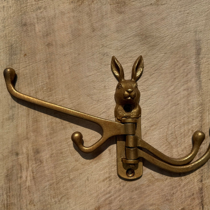 A vintage-style gold coat rack hook shaped like a rabbit head, mounted on a rustic wooden surface.