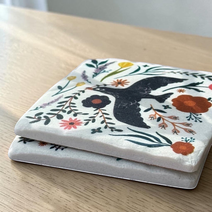 Two ceramic coasters with a bird and floral design on a wooden surface.