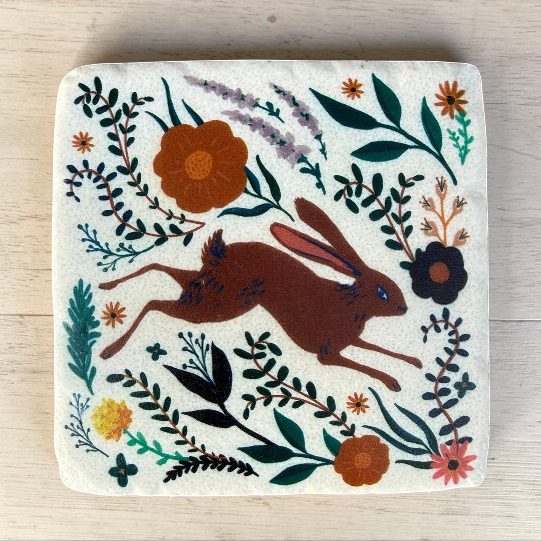 Decorative coaster with a rabbit and floral design on a wooden surface