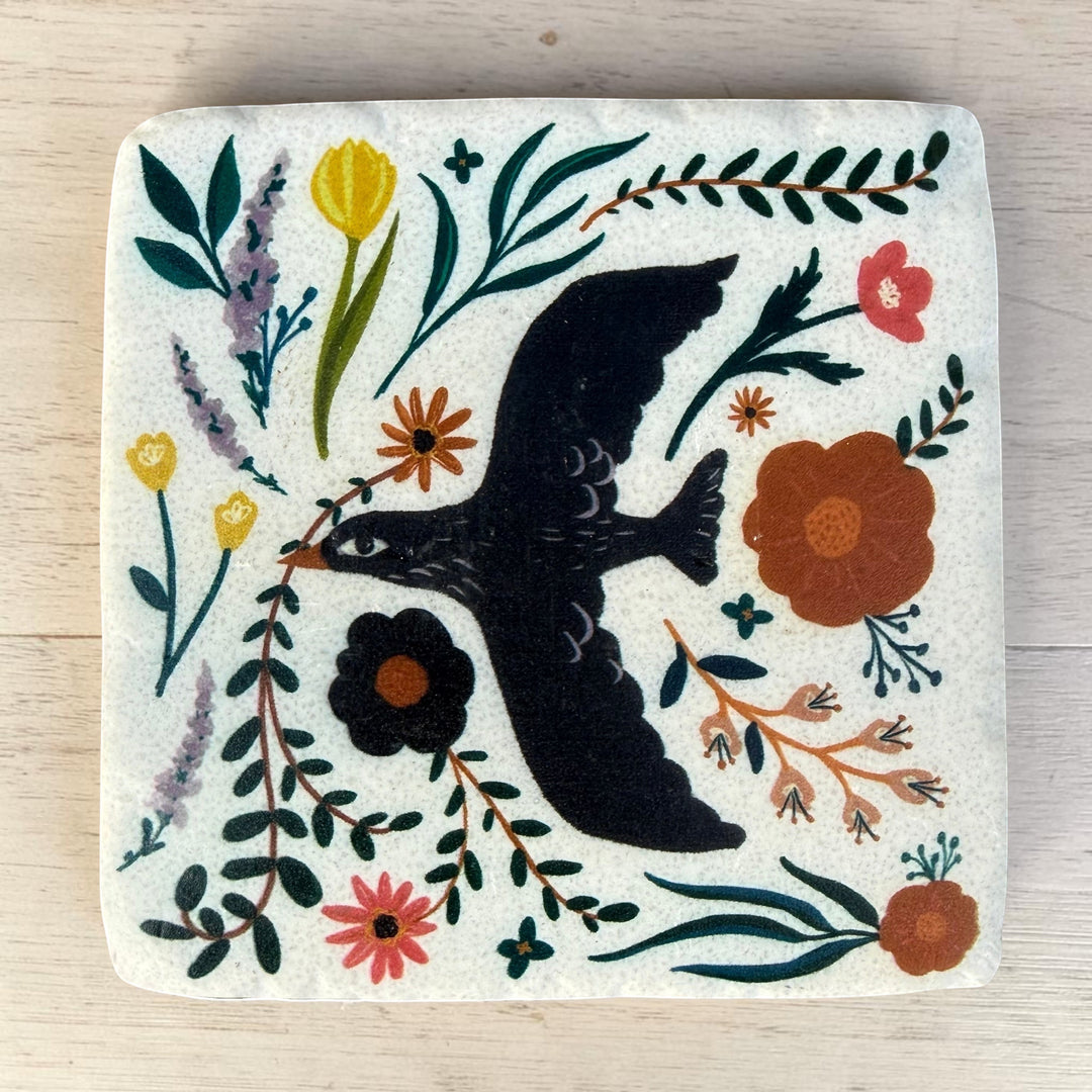 Square coaster with a bird and floral design on a wooden surface