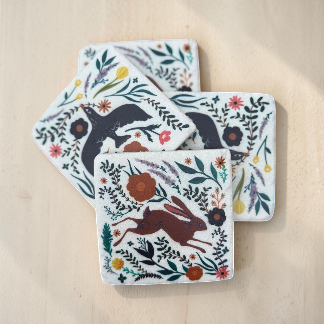 Set of four coasters with animal and floral designs on a wooden surface