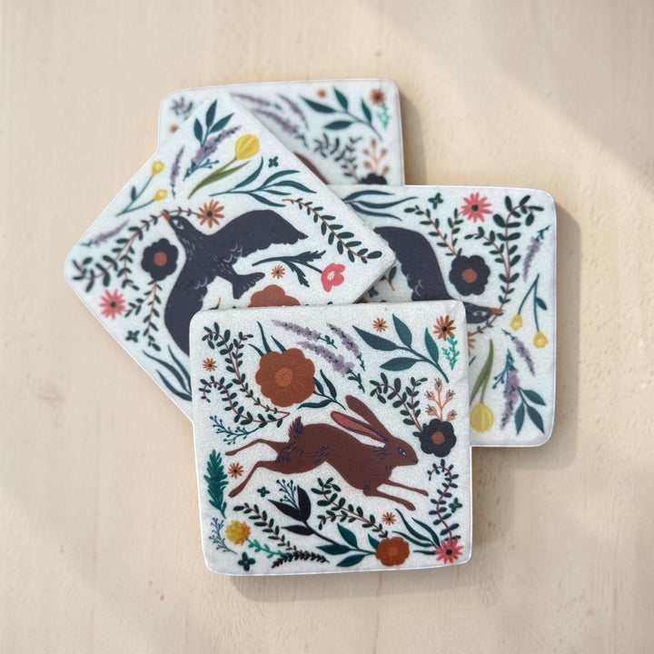 Set of four coasters with animal and floral designs on a wooden surface