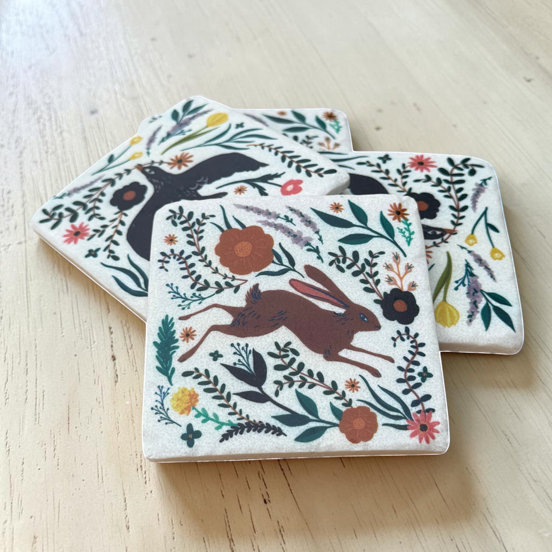Set of four coasters with animal and floral designs on a wooden surface