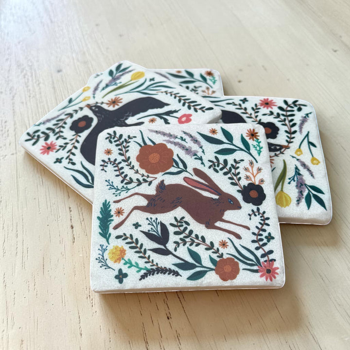 Set of four coasters with animal and floral designs on a wooden surface