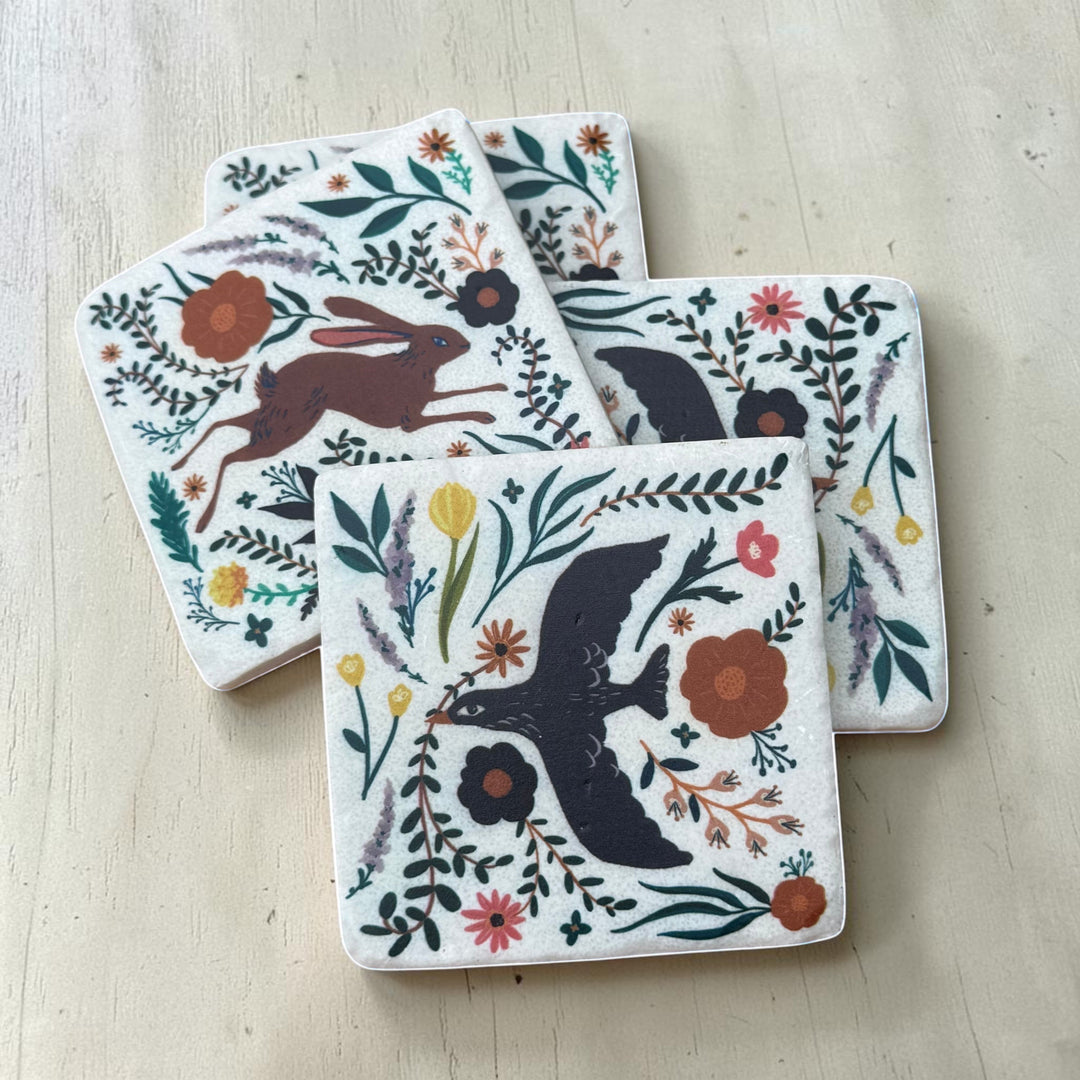 Set of four coasters with animal and floral designs on a light wooden surface