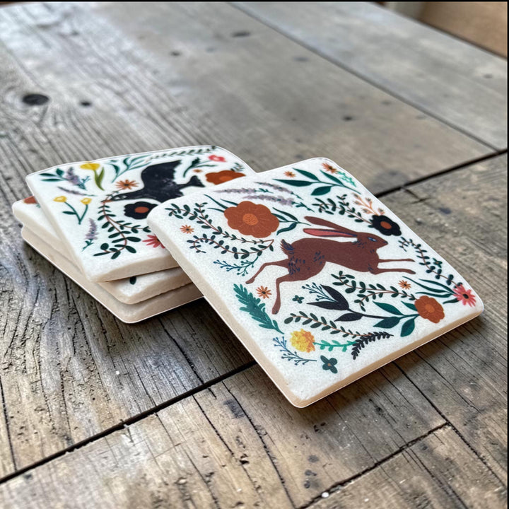 Set of four coasters with animal and floral designs on a wooden surface