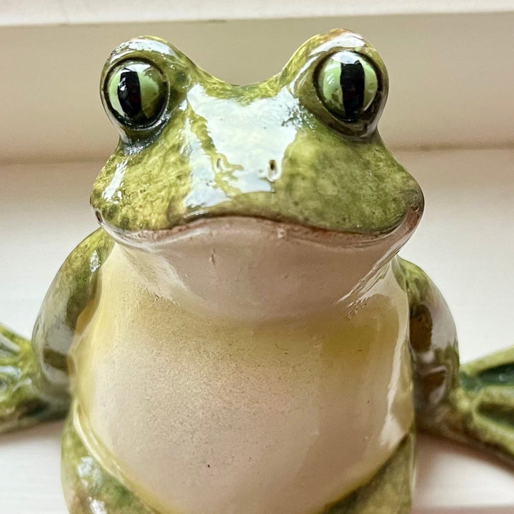 A glossy  frog resin figurine with green and beige colouring, featuring large detailed eyes and a smooth textured surface.