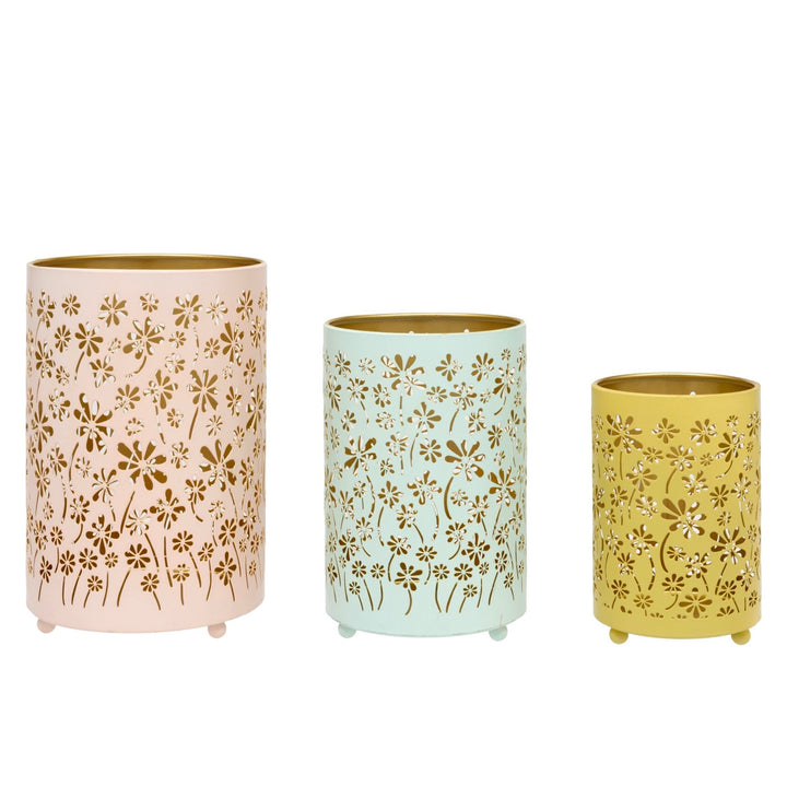 Three cylindrical metal candle holders with floral cutout patterns in pink, mint green, and mustard yellow, arranged by size on a white background.