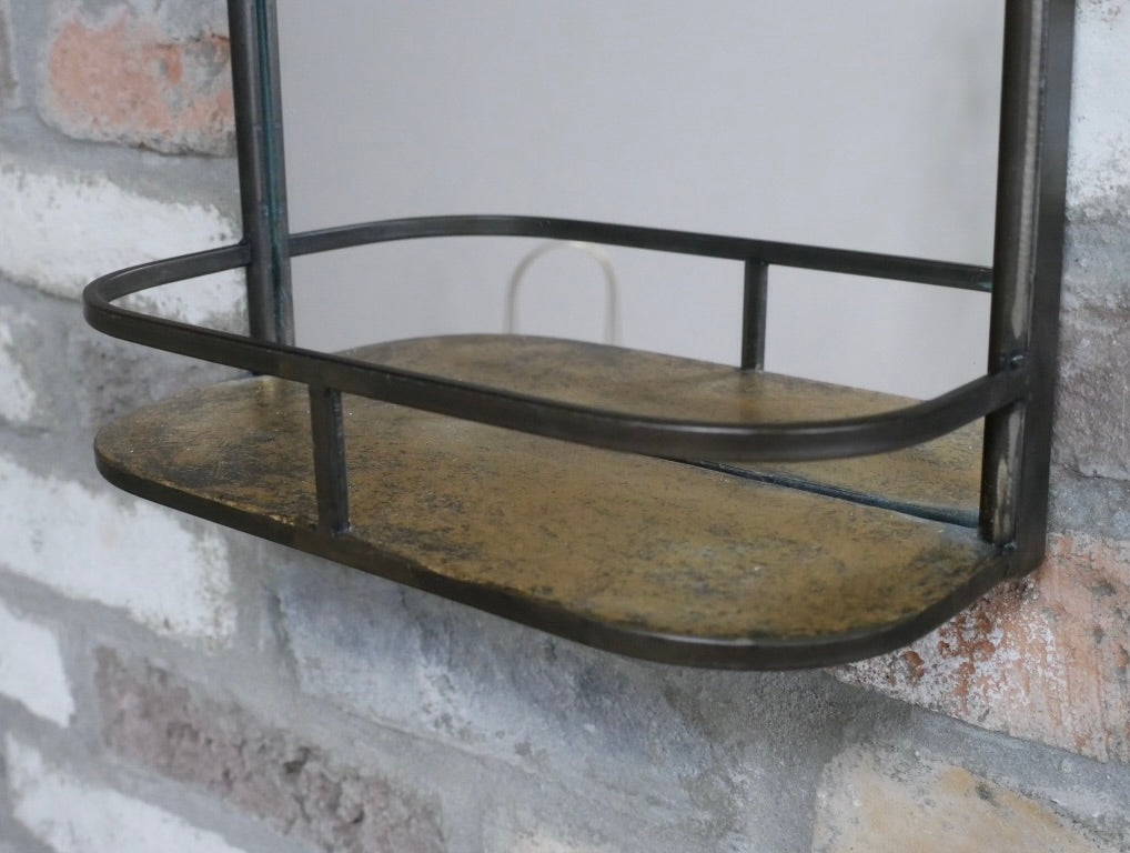 A rustic metal wall shelf with a distressed bronze finish, mounted on a white and gray brick wall.