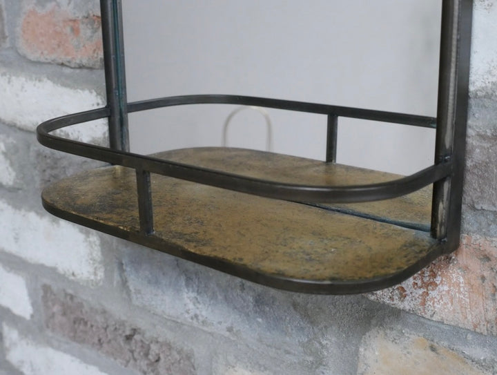 A rustic metal wall shelf with a distressed bronze finish, mounted on a white and gray brick wall.