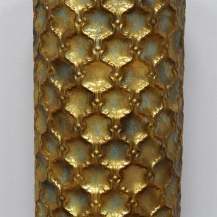 Decorative gold pillar with a textured pattern on a wooden floor against a grey wall.