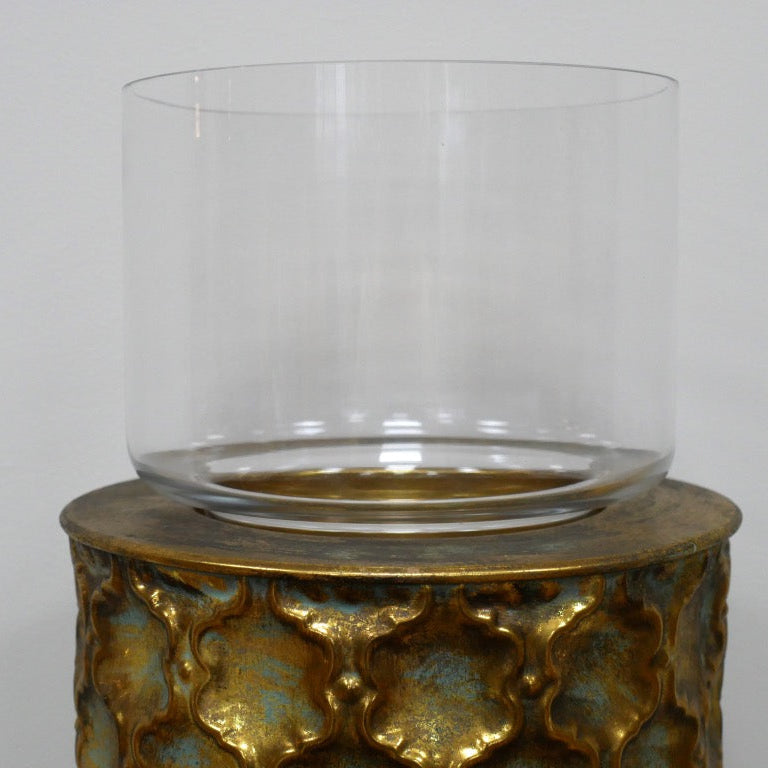 Decorative candle holder with gold patterned base and clear glass container on a grey background
