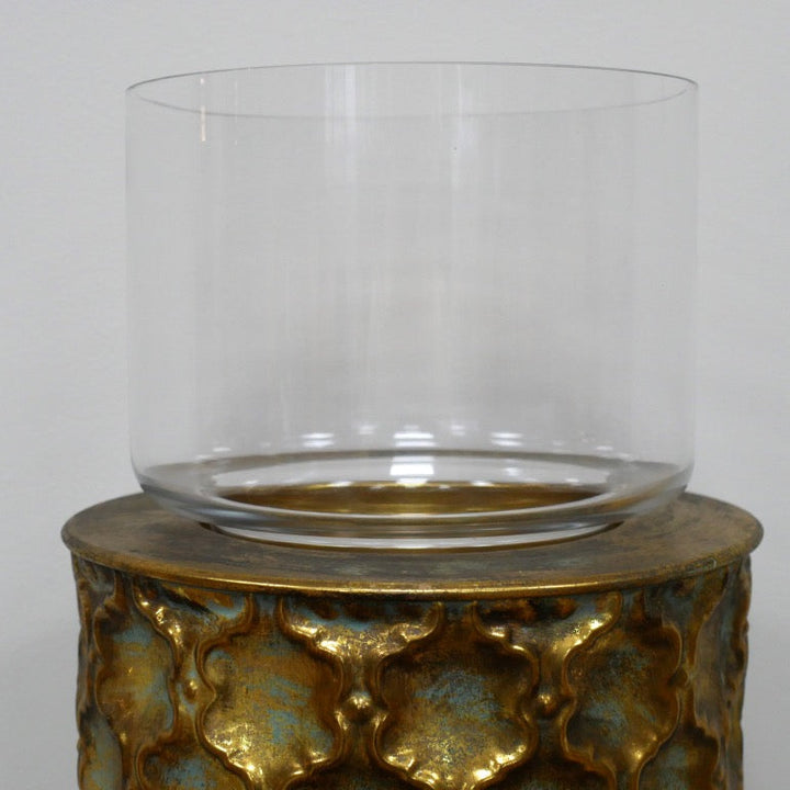 Decorative candle holder with gold patterned base and clear glass container on a grey background