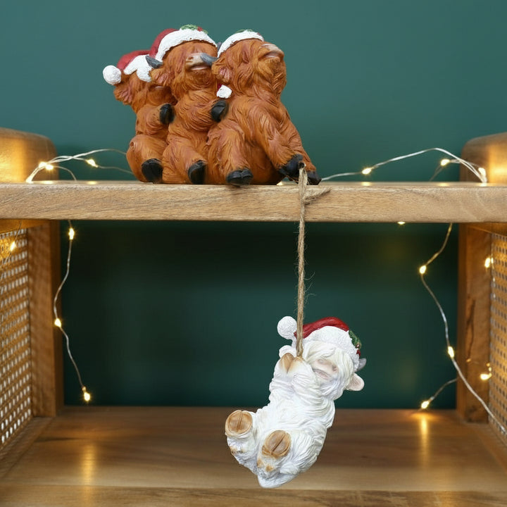 Decorative Christmas ornament - 3 brown cows with a white cow with a red Santa hat hanging from a wooden shelf.