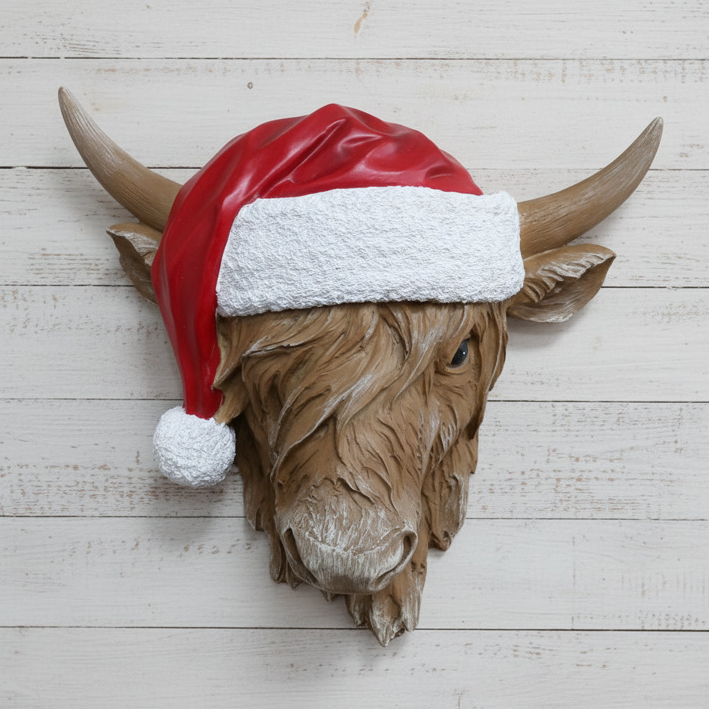 Decorative highland cow head wearing a Santa hat against a brick wall.