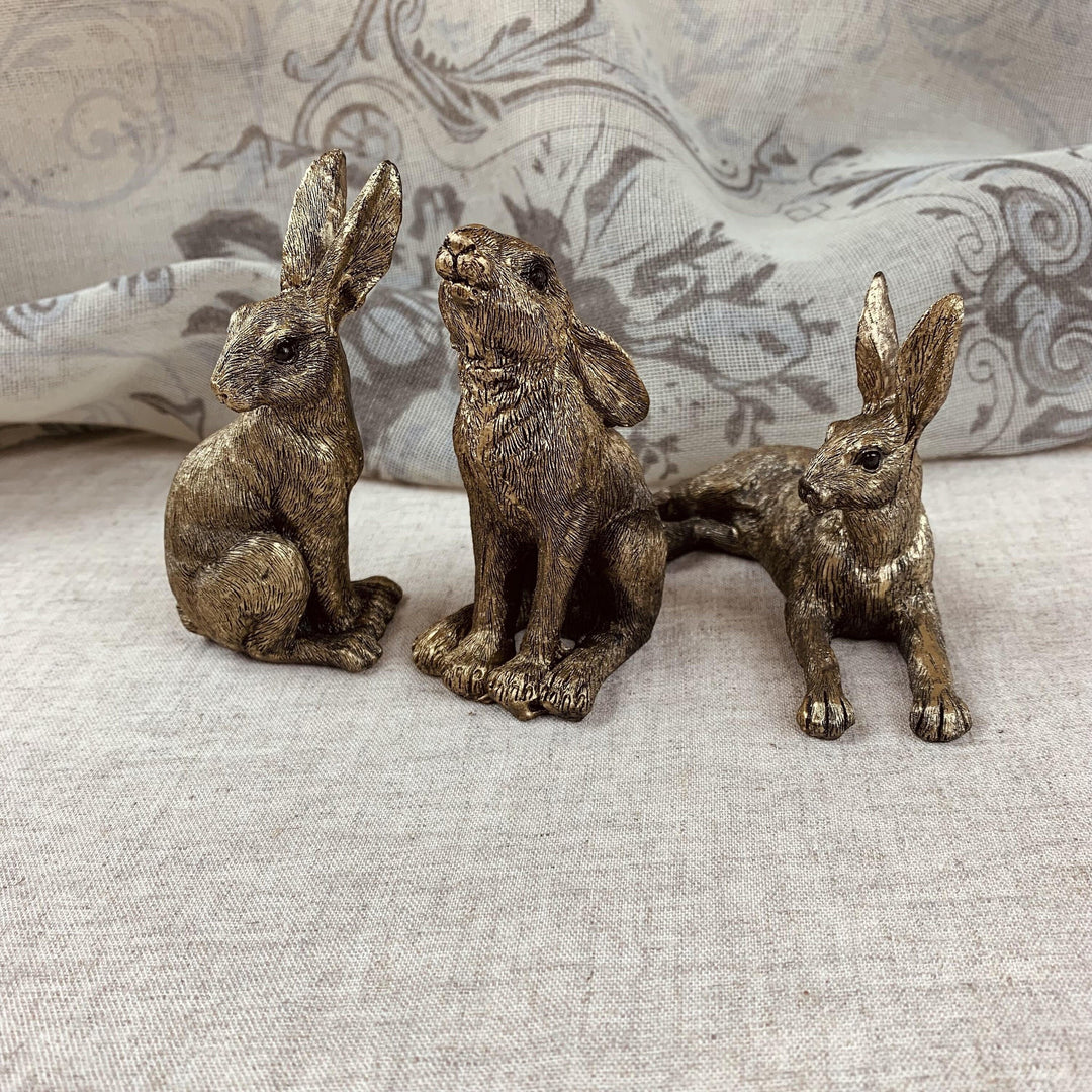Three bronze rabbit figurines on a textured surface with a patterned fabric background