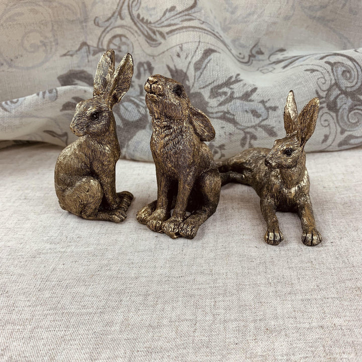 Three bronze rabbit figurines on a textured surface with a patterned fabric background