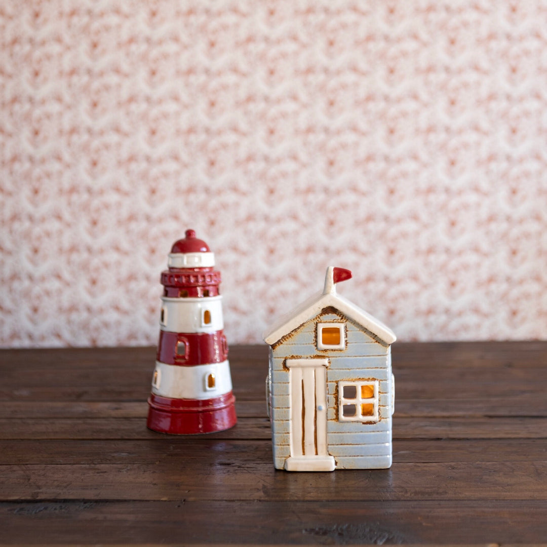 Decorative lighthouse and cottage figurines on a wooden surface with a patterned wall background.