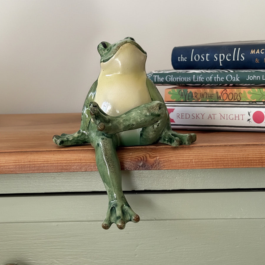 frog shaped figurine sitting on a wooden table with a stack of books in the background