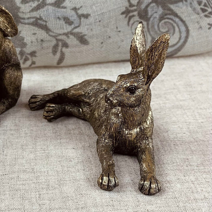 Bronze rabbit figurine on a textured surface with a floral-patterned fabric background