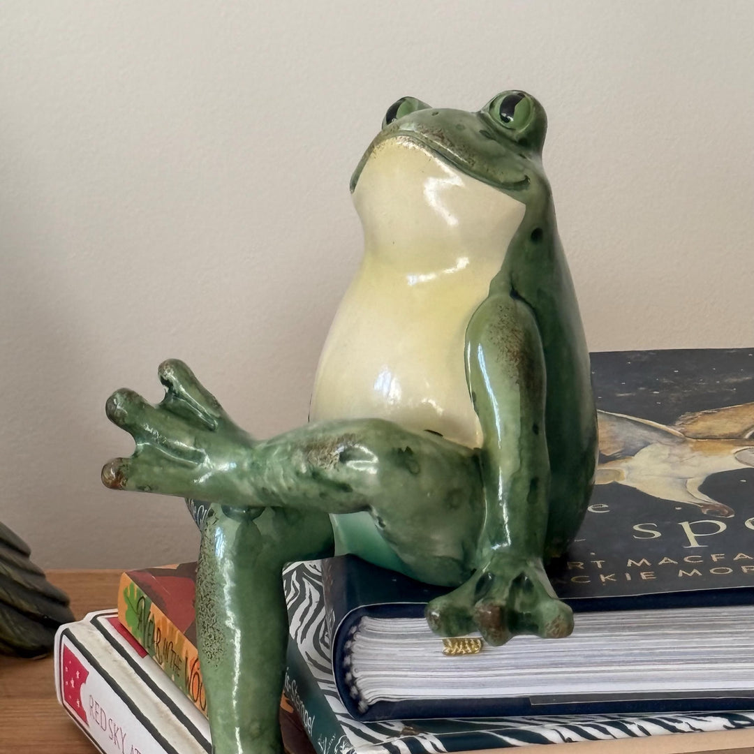 Green frog figurine on a stack of books with a plain background