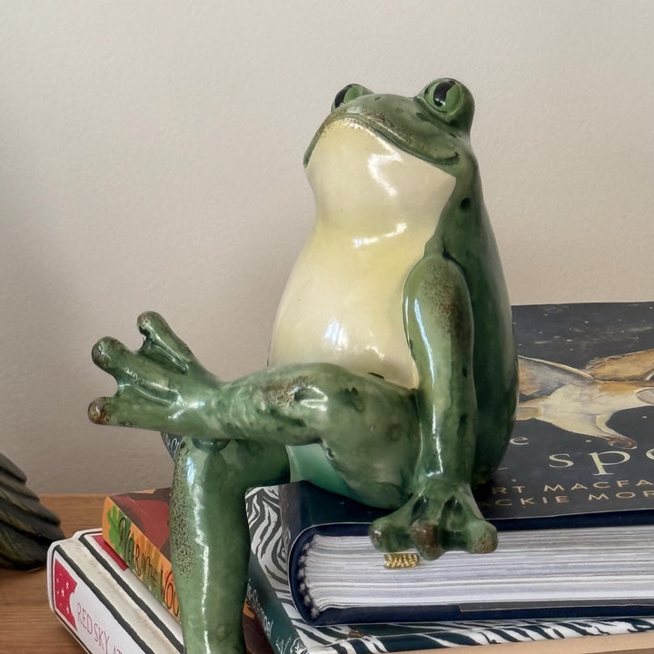 Green frog figurine on a stack of books with a plain background